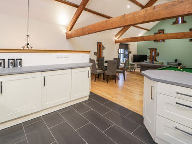 A kitchen area with white cabinets and a gray countertop opening to a dining and living room with wooden beams at The Barn by Lyons in Talybont near Barmouth