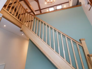 An interior space with a wooden staircase and railing a blue wall and exposed wooden ceiling beams at The Barn by Lyons in Talybont near Barmouth