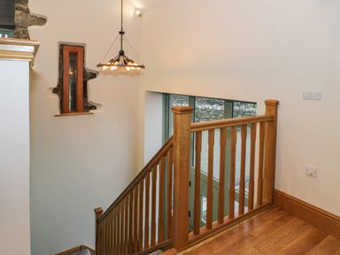 A wooden stair railing leading down with a pendant light and narrow window at The Barn by Lyons Talybont near Barmouth