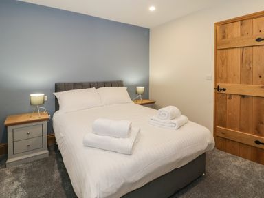 A bedroom with a double bed two bedside tables with lamps wooden door at The Barn by Lyons in Talybont near Barmouth
