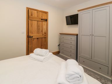 A bedroom with a wooden door gray wardrobe and dresser and a bed with folded towels at The Barn by Lyons in Talybont near Barmouth