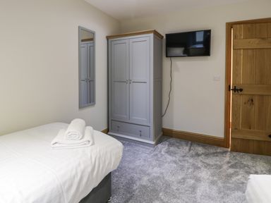 A bedroom with a bed and towels a mirror a gray wardrobe a wall-mounted television and a wooden door at The Barn by Lyons in Talybont near Barmouth