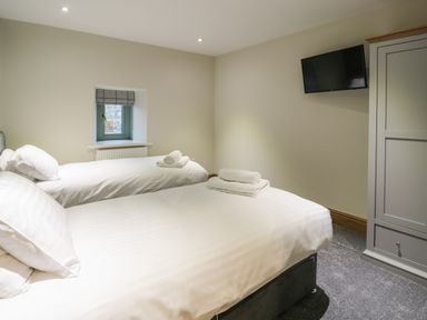 A bedroom with two single beds each with folded towels a small window a wall mounted television and a wardrobe at The Barn by Lyons in Talybont near Barmouth