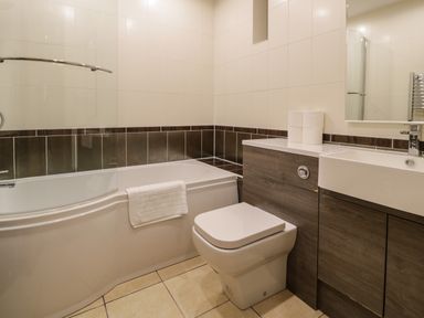 A bathroom with a bathtub toilet sink and wooden cabinets at The Barn by Lyons in Talybont near Barmouth