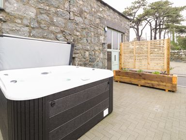 An outdoor patio area with a hot tub wooden planter and stone wall at The Barn by Lyons in Talybont near Barmouth