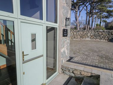A pale green door with glass panels next to a stone wall and paved driveway at The Barn by Lyons in Talybont near Barmouth