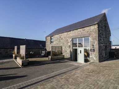 Stone building with glass doors and wooden planters on paved area outside at The Barn by Lyons in Talybont near Barmouth