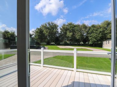 A balcony with glass railing overlooking a green lawn trees and mobile homes at 7 The Oaks in Long Preston near Hellifield