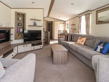 A living room with a grey sofa and cushions a wooden coffee table a television and dining table at 7 The Oaks Long Preston near Hellifield