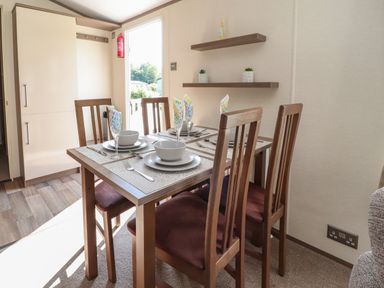 A dining area with a table set for four with chairs and shelves on the wall at 7 The Oaks Long Preston near Hellifield