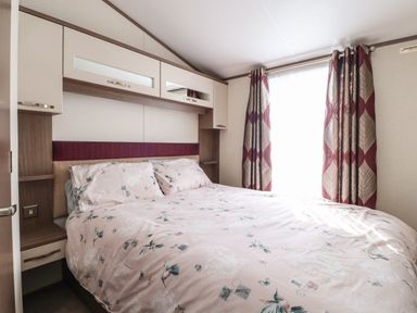 A bedroom with a double bed and floral bedding next to a window with patterned curtains at 7 The Oaks in Long Preston near Hellifield