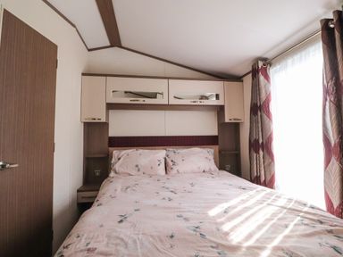 A bedroom with a bed and overhead cabinets beside a window with patterned curtains at 7 The Oaks in Long Preston near Hellifield