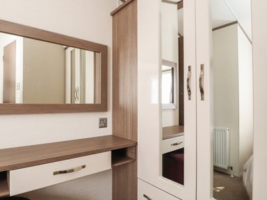 A bedroom corner with a wooden dressing table and mirror next to a wardrobe with mirrored doors at 7 The Oaks Long Preston near Hellifield