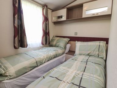 A bedroom with two single beds and patterned bedding under a window with curtains at 7 The Oaks in Long Preston near Hellifield