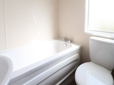 A bathroom with a bathtub a toilet and a frosted window at 7 The Oaks in Long Preston near Hellifield