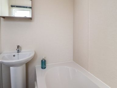 A bathroom with a pedestal sink mirror above and a bathtub with liquid soap at 7 The Oaks Long Preston near Hellifield