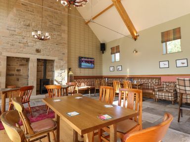 An interior dining area with wooden tables and chairs a stone fireplace and a mounted television at 7 The Oaks Long Preston near Hellifield