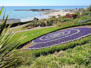 A coastal park with flower beds and pathways overlooking a beach and harbor at Sir George Baker Cabin in Uplyme
