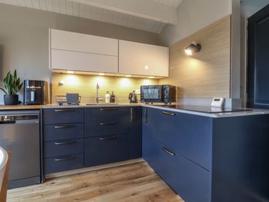 A kitchen with blue lower cabinets white upper cabinets wooden floor and various appliances at Sir George Baker Cabin in Uplyme