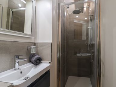 A bathroom with a sink, mirror, towel, soap dispenser and a glass shower enclosure at Sir George Baker Cabin in Uplyme