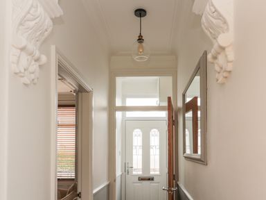 A hallway with a white front door a light fixture mirror and decorative corbels at 18 Acklington Road in Amble