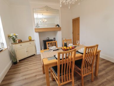 A dining room with a wooden table set for four and a sideboard with flowers at 18 Acklington Road in Amble