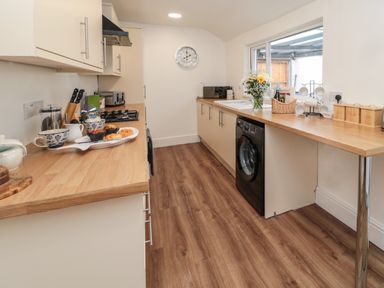 A kitchen with wooden countertops, cream cabinets, a washing machine, a stove, and a window with a flower vase on the counter at 18 Acklington Road Amble