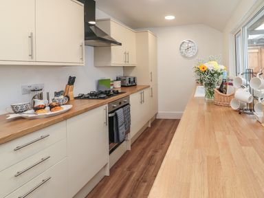 A kitchen with wooden countertops cabinets a stove a toaster flowers and mugs on a stand at 18 Acklington Road in Amble