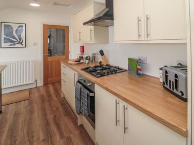 A kitchen with wooden countertop white cabinets a gas stove an oven a toaster and a wooden door at 18 Acklington Road Amble