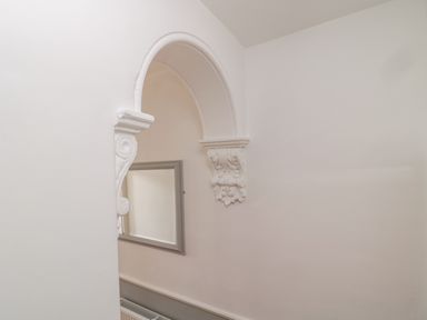 A white wall with an arched decorative opening and a rectangular mirror and a radiator below at 18 Acklington Road in Amble