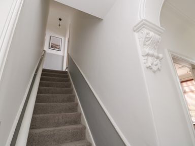 A staircase with carpeted steps and a handrail leading to a hallway with a framed picture and a doorway at 18 Acklington Road in Amble