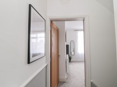 A hallway with a wooden door open to a carpeted room with a tall mirror and a potted plant at 18 Acklington Road in Amble
