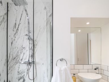 A bathroom with a shower area featuring a rainfall showerhead and glass door next to a sink with a round basin mirror towel ring and soap dispenser at 18 Acklington Road in Amble
