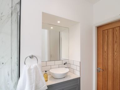 A bathroom sink with a round white basin and soap dispenser next to a wooden door at 18 Acklington Road in Amble