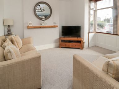 A living room with two beige sofas a wall mirror a wooden shelf with decorations a television on a wooden stand and windows with blinds at 18 Acklington Road in Amble