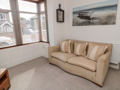 A beige sofa with three cushions under a boat painting next to a window with blinds at 18 Acklington Road in Amble