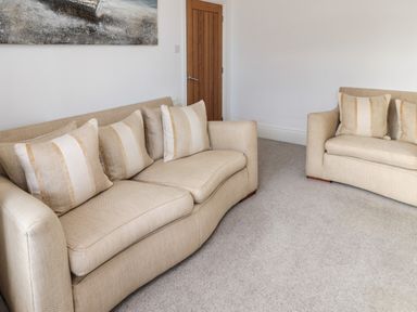 A room with two beige sofas with striped cushions and a wooden door at 18 Acklington Road in Amble