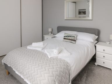 A bedroom with a double bed pillows bedside tables lamps and a mirror at 18 Acklington Road in Amble