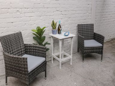 Two wicker chairs with cushions and a small white table with plants wine bottle and glasses against a brick wall at 18 Acklington Road in Amble