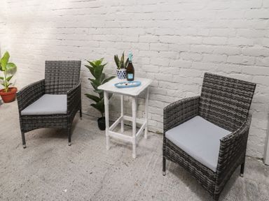 Two wicker chairs with cushions around a small white table with plants and a bottle on it on a concrete floor at 18 Acklington Road in Amble