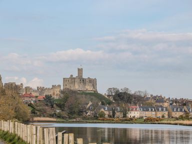 A river with houses and a large stone castle on a hill in the background at 18 Acklington Road in Amble