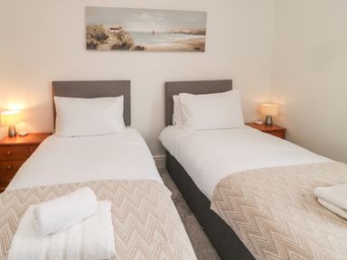 A bedroom with two single beds each with white bedding beside wooden nightstands with lamps at 18 Acklington Road in Amble