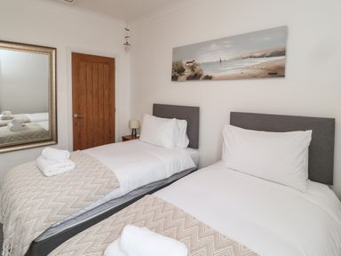 A bedroom with two single beds white bedding a wooden door and a painting above the beds at 18 Acklington Road in Amble