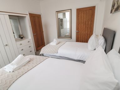 A bedroom with two single beds white bedding wooden doors and a white wardrobe at 18 Acklington Road in Amble