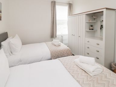 A bedroom with two single beds a white wardrobe with drawers and a window with curtains at 18 Acklington Road in Amble
