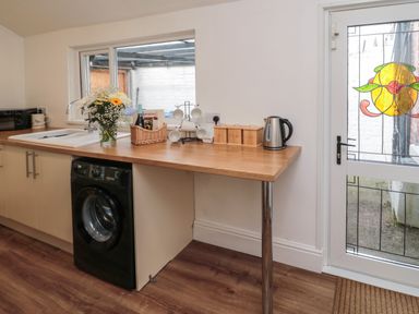 A kitchen with a washing machine sink flowers kettle and a door with stained glass at 18 Acklington Road in Amble