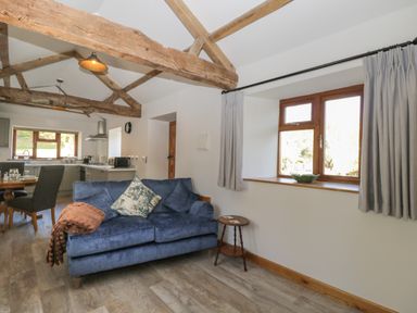 A living area with a blue sofa and wooden beams on the ceiling near a kitchen and dining table at Keepers Barn in Bromyard