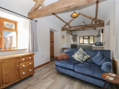A living room with wooden beams a blue sofa and a wooden cabinet at Keepers Barn in Bromyard