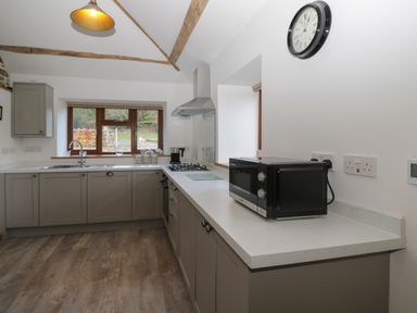 A kitchen with gray cabinets a microwave on the counter a gas stove a sink and a window showing trees at Keepers Barn in Bromyard