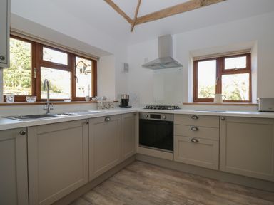 A kitchen with wooden framed windows a stainless steel sink gas stove oven and beige cabinets at Keepers Barn in Bromyard